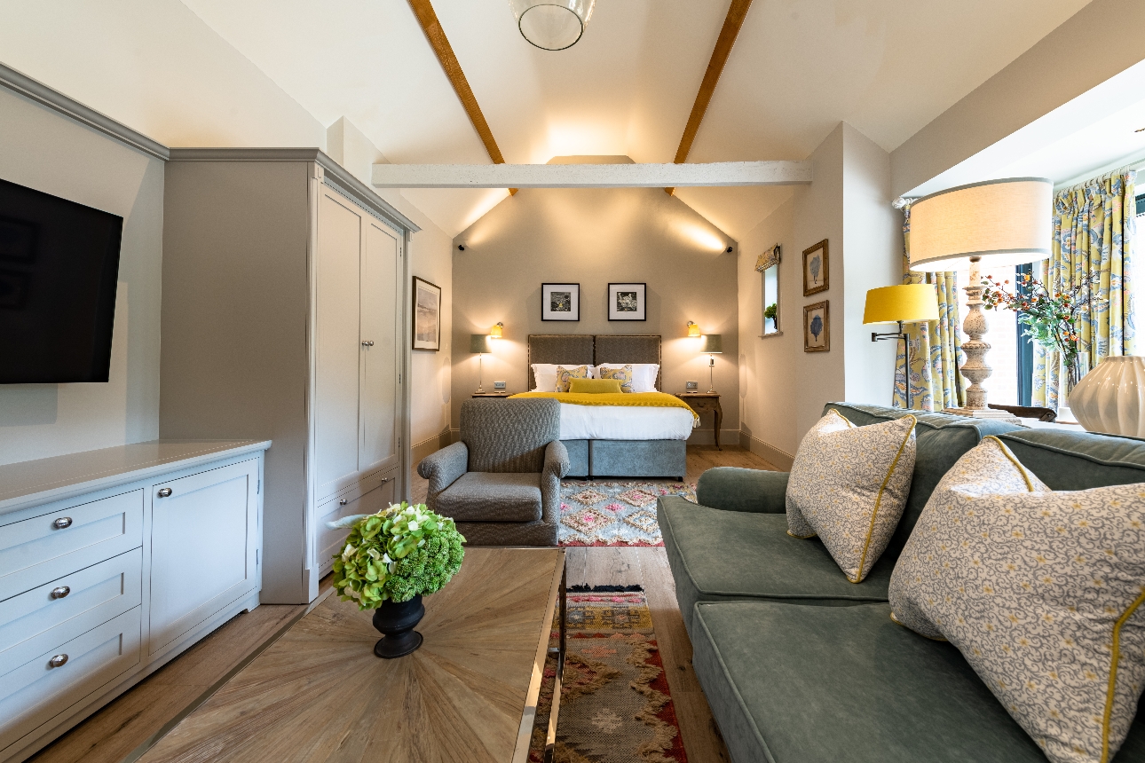 large suite, neutral tones, bed, sofa, armchair, tv beams on ceiling